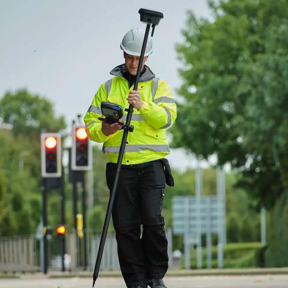 Land surveyor wearing high visibility safety vest using GNSS receiver on traffic street.